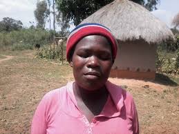 woman in pink shirt outside thatched hut wearing hat